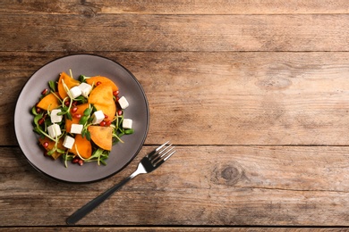 Photo of Delicious persimmon salad served on wooden table, flat lay. Space for text