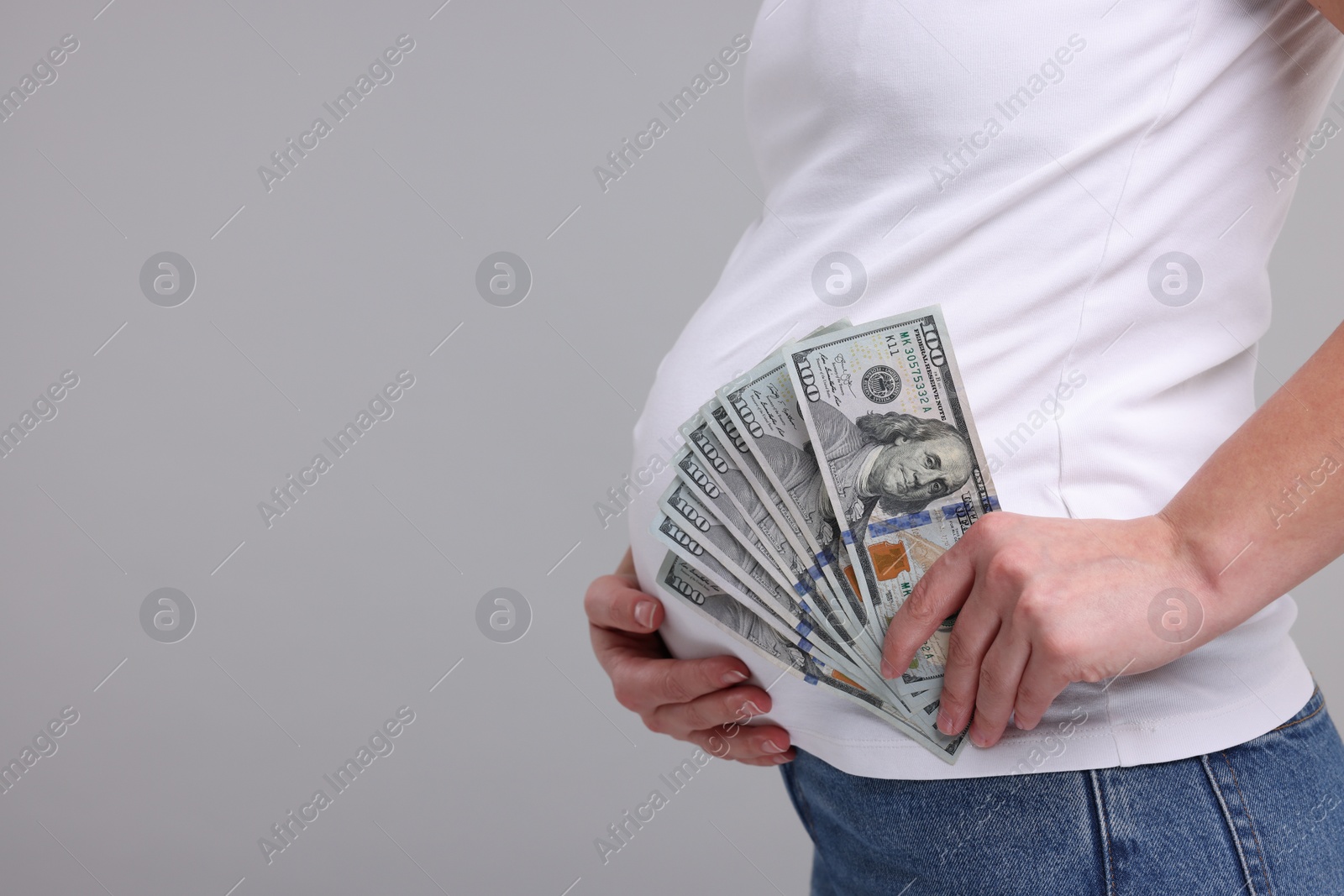 Photo of Surrogate mother. Pregnant woman with dollar banknotes on light grey background, closeup. Space for text