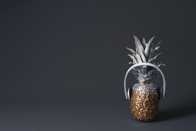 Photo of Pineapple with headphones on dark background. Space for text