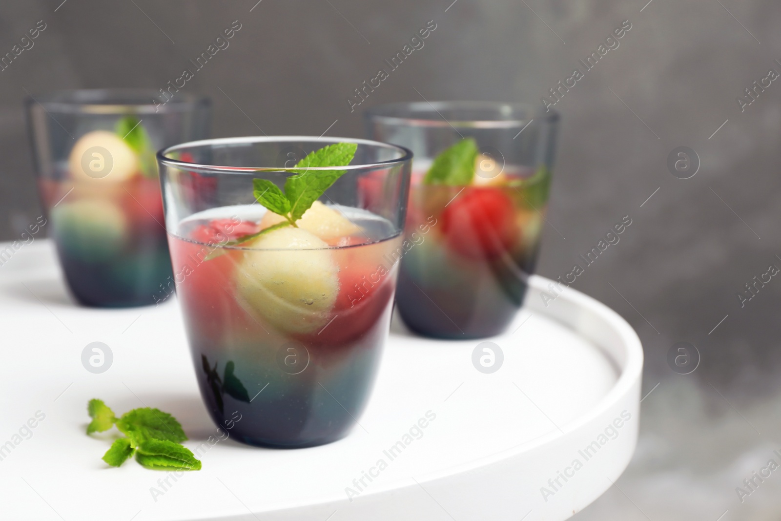 Photo of Glasses with tasty melon and watermelon ball drink on light table against color wall