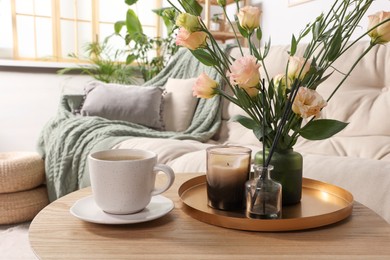 Photo of Beautiful flowers and cup of drink on wooden coffee table in living room