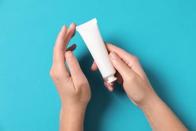 Woman with tube of hand cream on light blue background, top view