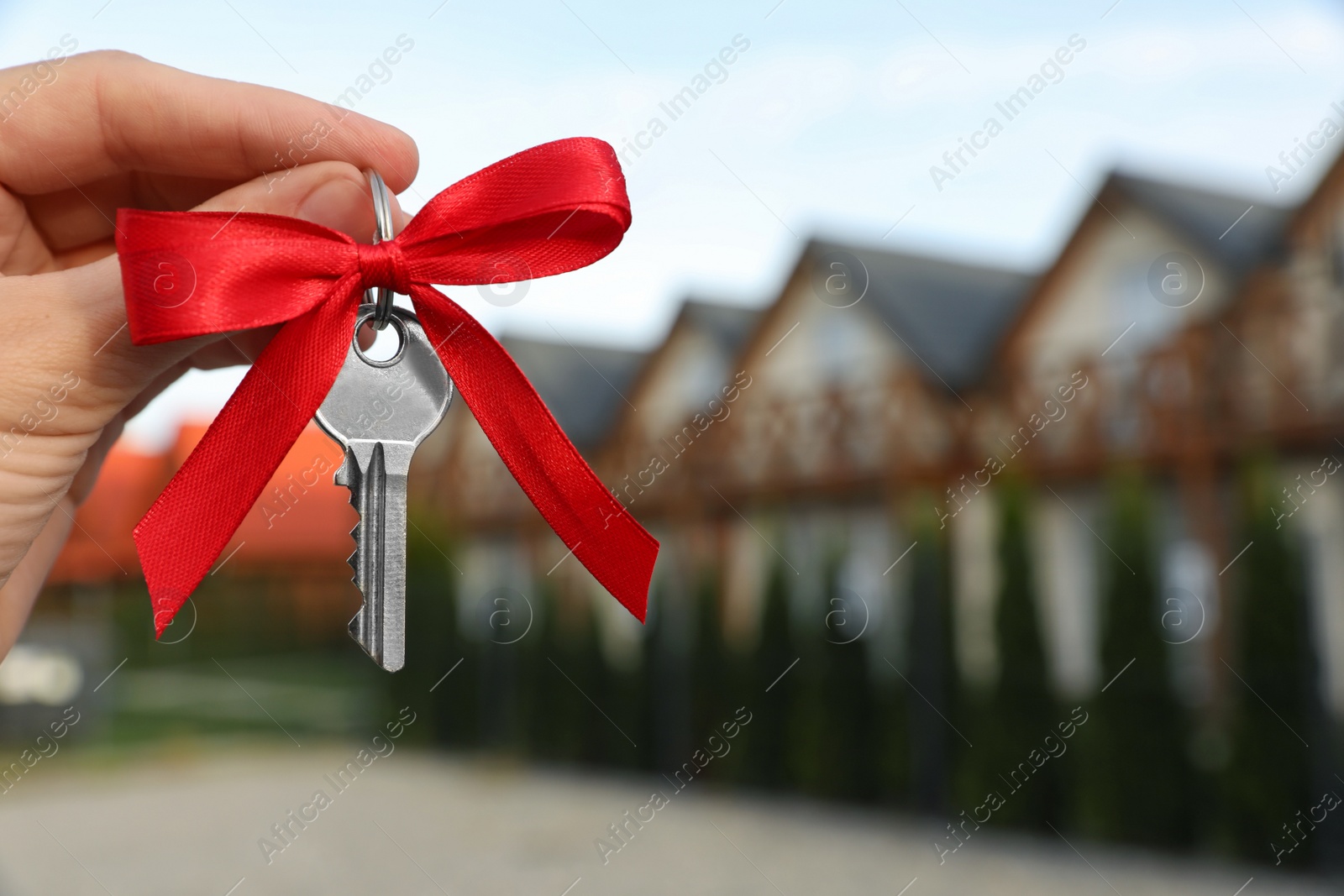 Photo of Woman holding key with bow near house outdoors, closeup. Space for text