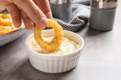 Woman dipping homemade crunchy fried onion ring in sauce on table, closeup