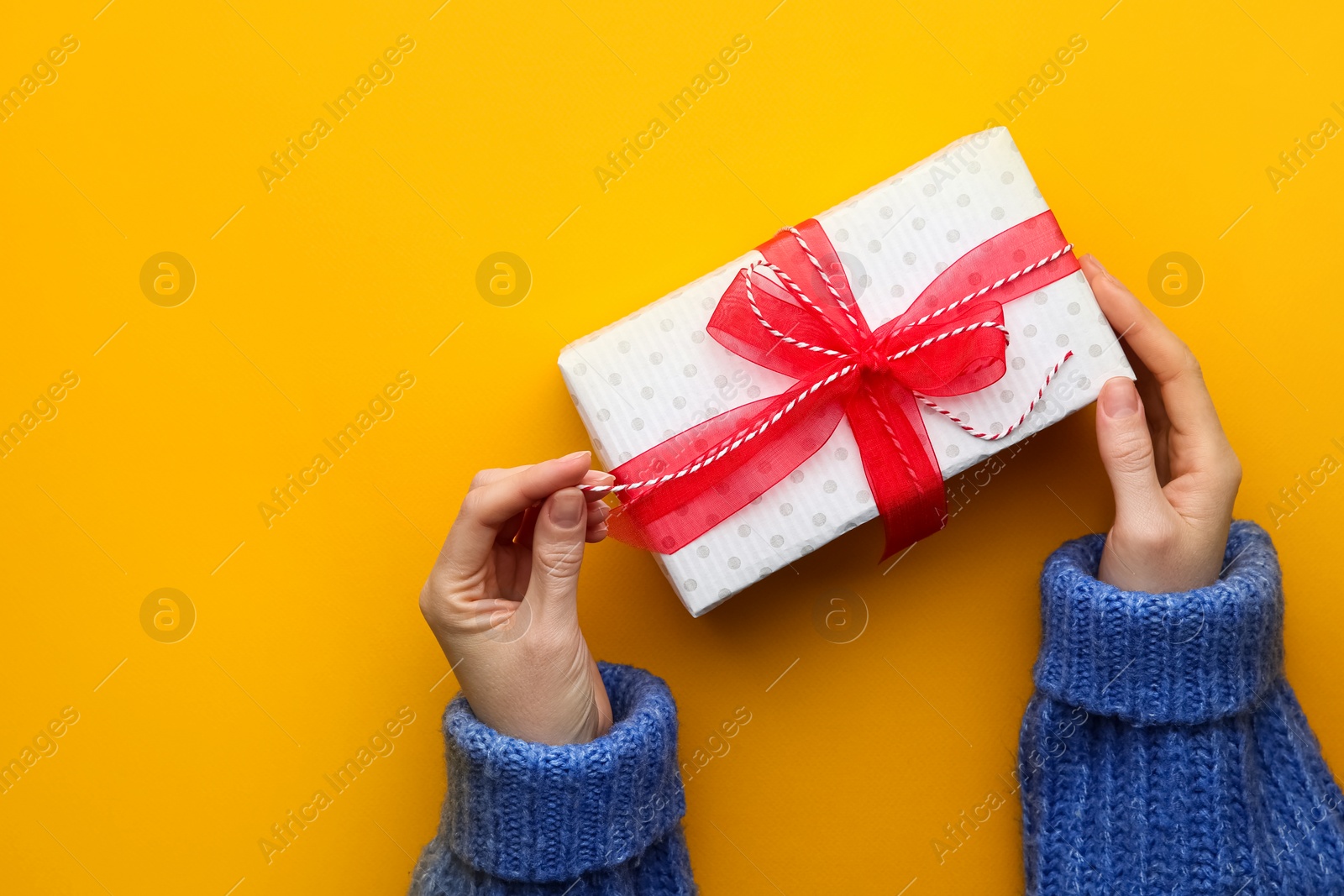 Photo of Woman holding Christmas gift box on orange background, top view