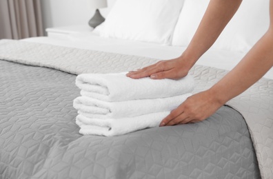Photo of Young maid putting stack of fresh towels on bed in hotel room, closeup