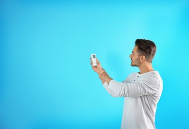 Photo of Young man with air conditioner remote on color background