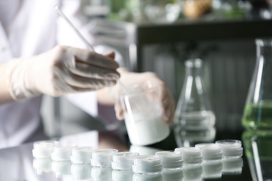 Photo of Scientist working in cosmetic laboratory, focus on jars with cream