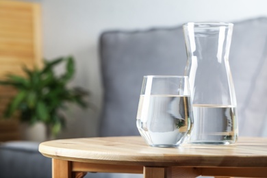 Photo of Jug and glass of water on wooden table in room, space for text. Refreshing drink