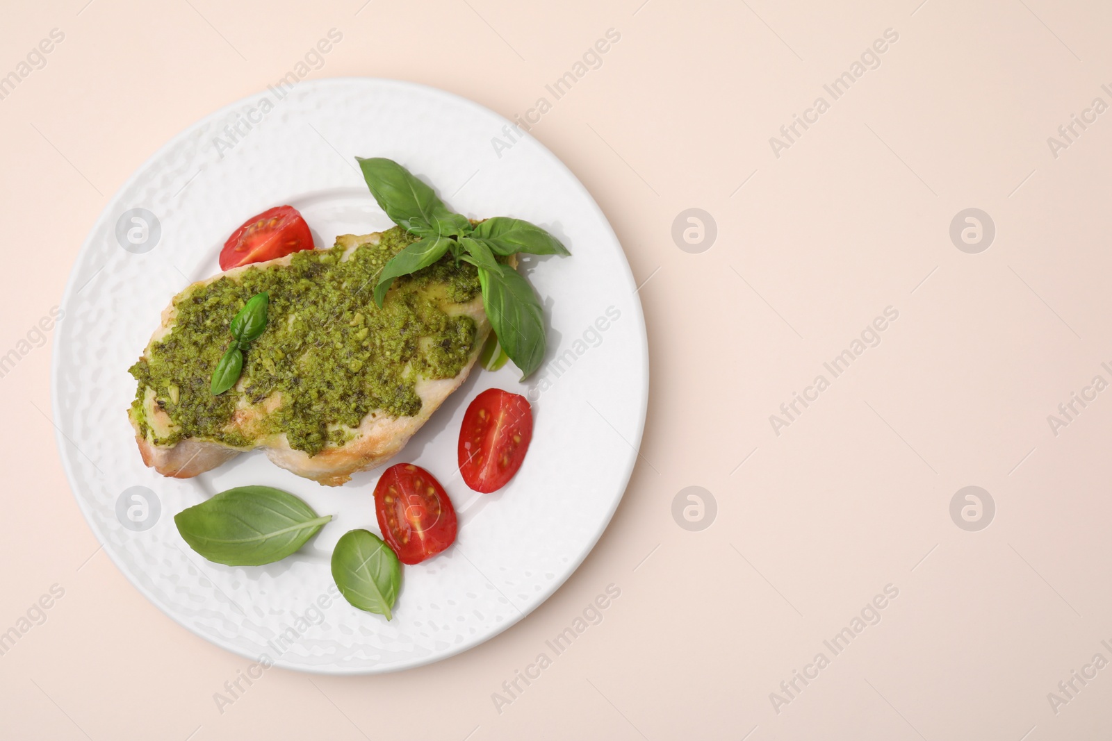 Photo of Delicious chicken breast with pesto sauce, tomatoes and basil on beige table, top view. Space for text