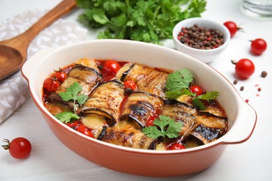 Tasty eggplant rolls with tomatoes, cheese and parsley in baking dish on white wooden table