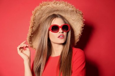 Photo of Young woman wearing stylish sunglasses and hat on red background
