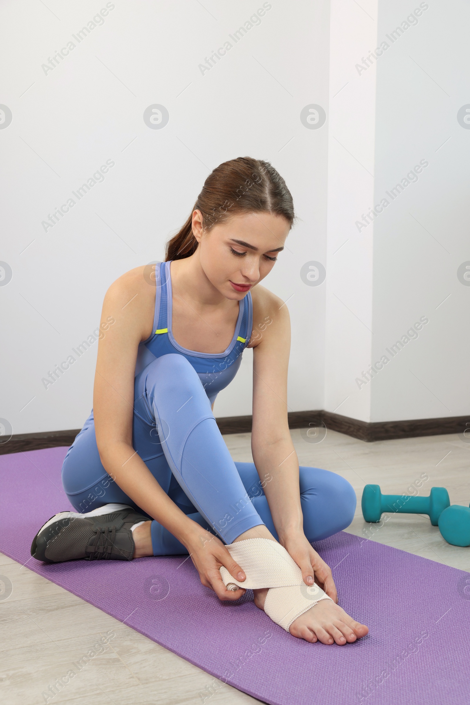 Photo of Woman wrapping foot in medical bandage on yoga mat indoors