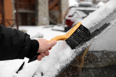 Photo of Man cleaning car windshield from snow with brush outdoors, closeup