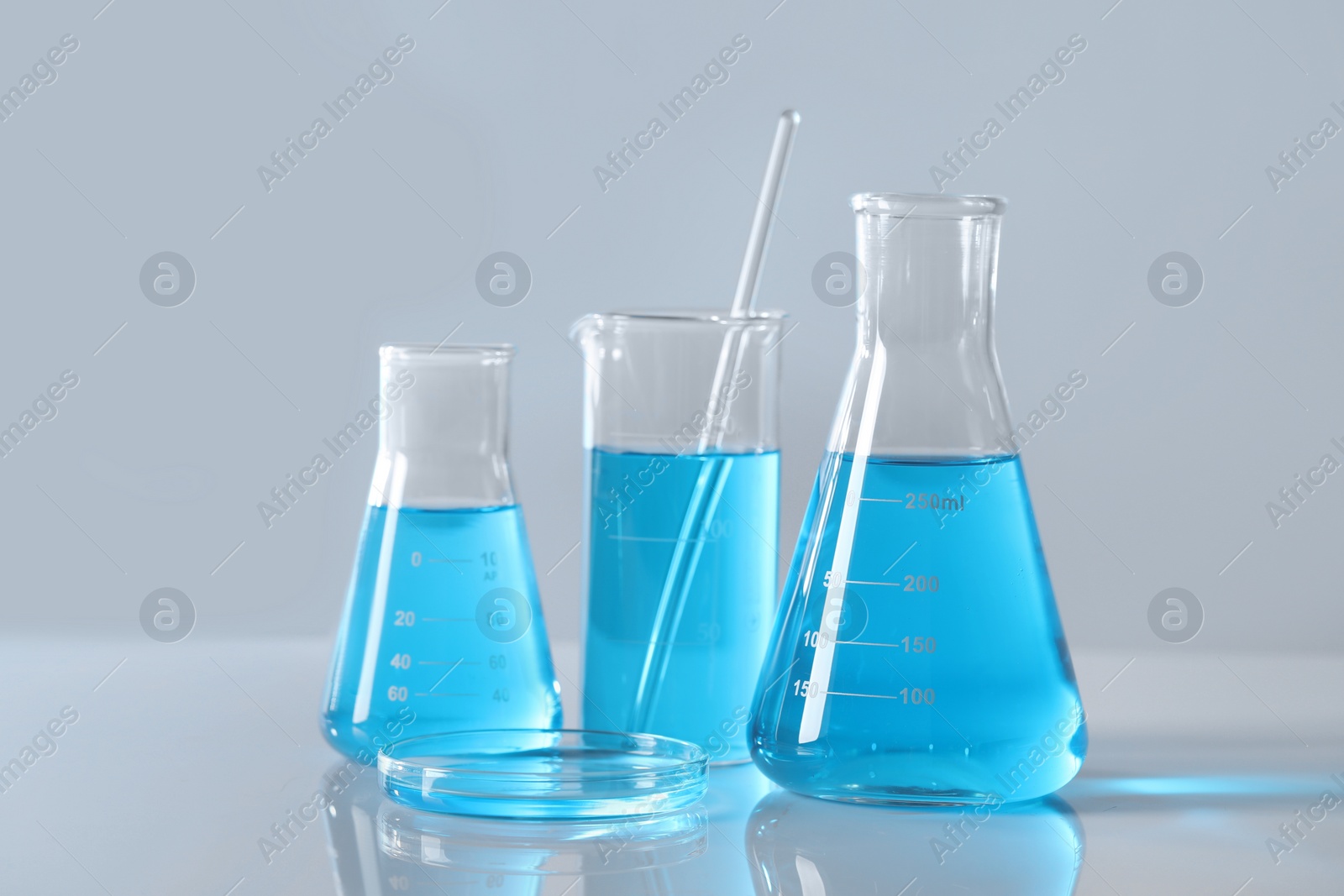 Photo of Different laboratory glassware with light blue liquid on table