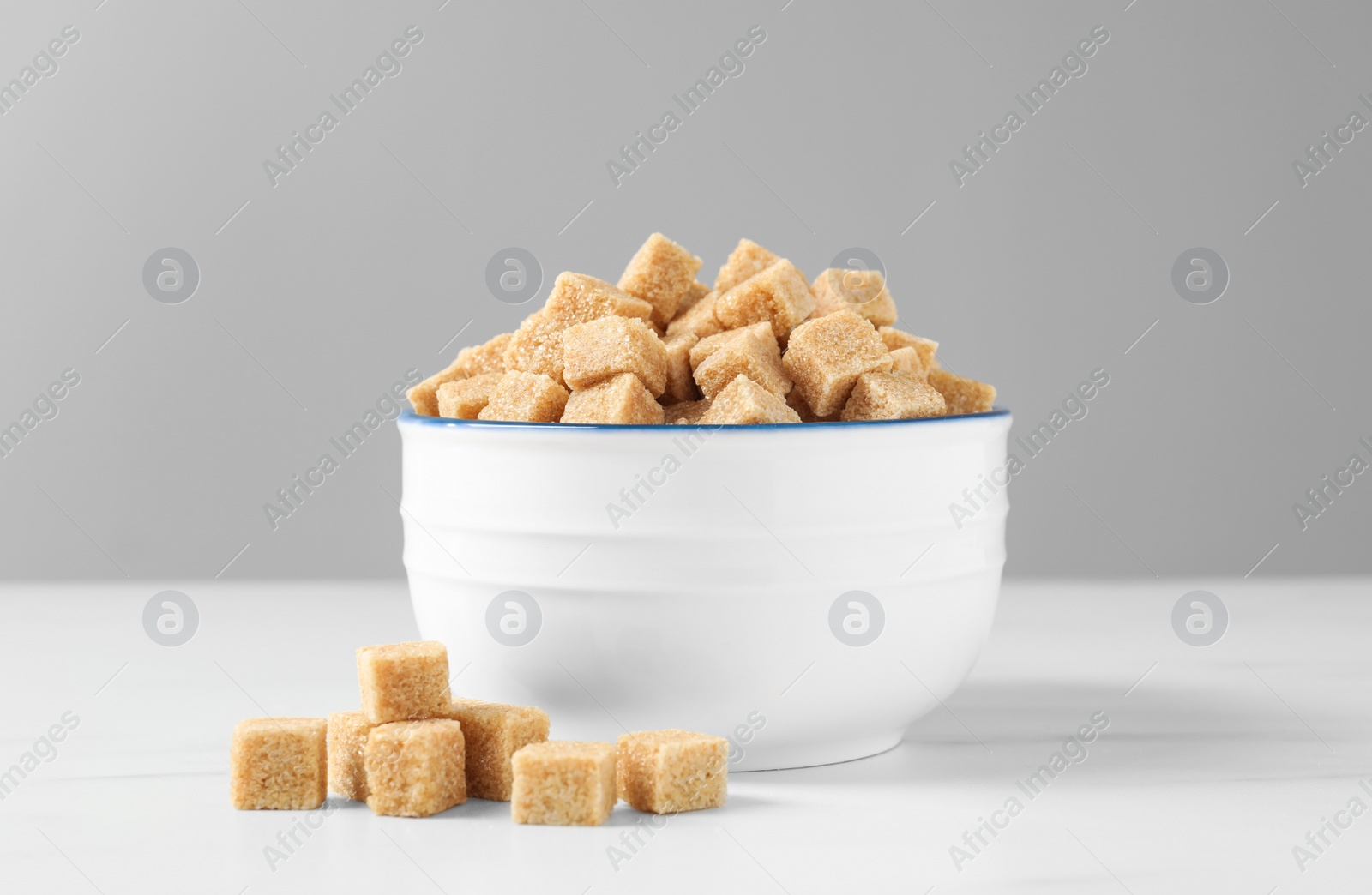 Photo of Bowl with brown sugar cubes on white table