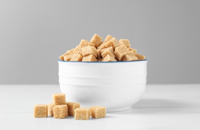 Photo of Bowl with brown sugar cubes on white table