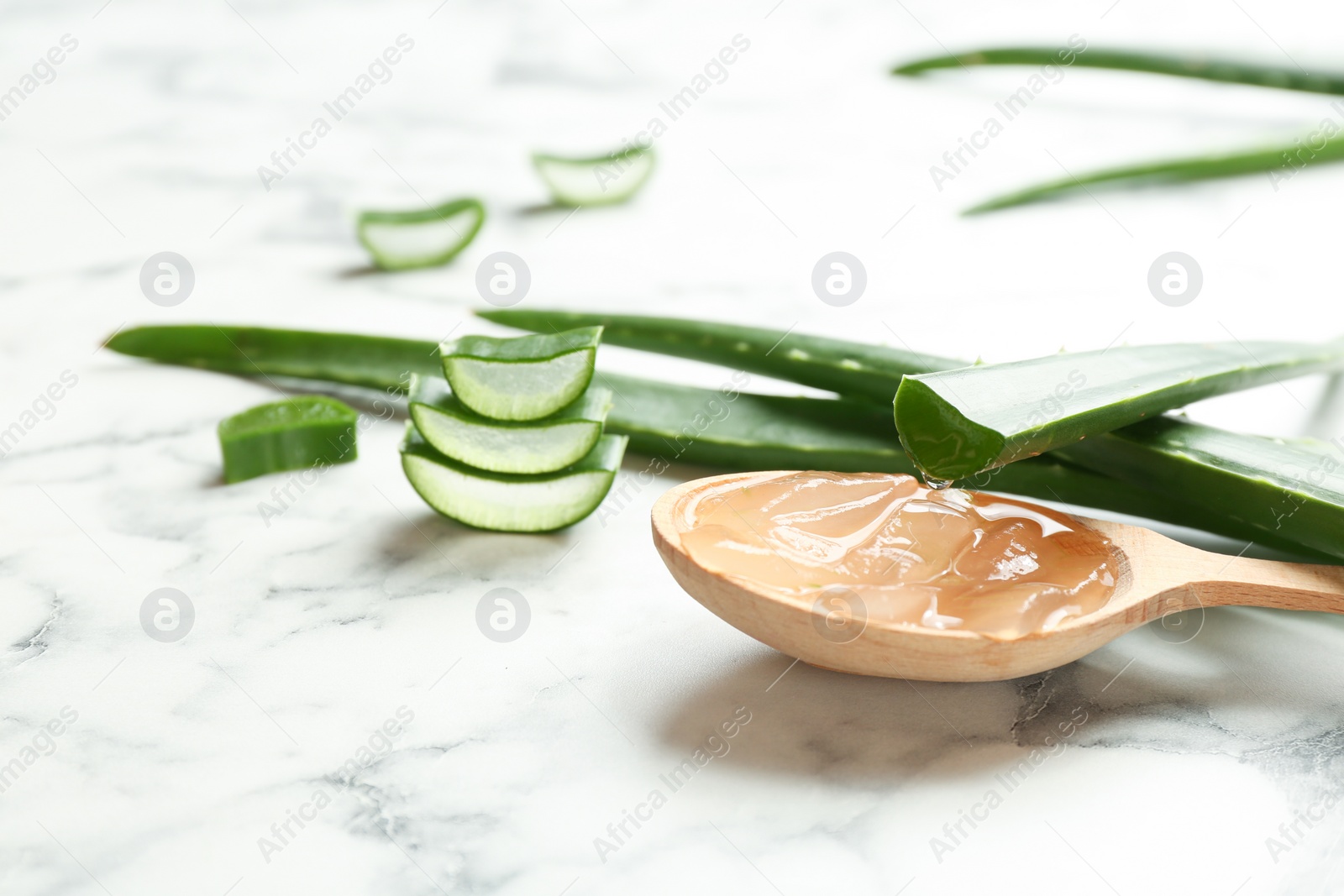 Photo of Wooden spoon with aloe vera gel and green leaves on marble table. Space for text