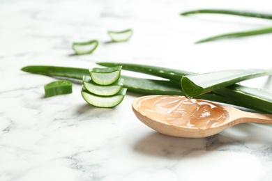 Wooden spoon with aloe vera gel and green leaves on marble table. Space for text