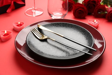 Place setting with heart shaped candles, gift box and bouquet of roses on red table, closeup. Romantic dinner