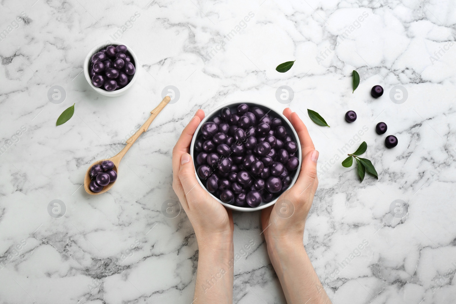 Photo of Woman holding bowl with tasty acai berries at white marble table, top view