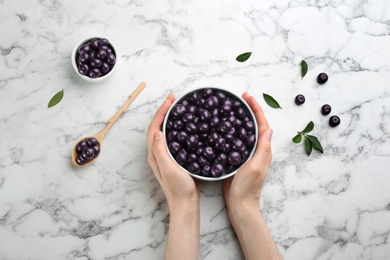 Photo of Woman holding bowl with tasty acai berries at white marble table, top view