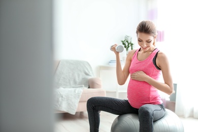 Photo of Young pregnant woman doing exercises with dumbbell at home