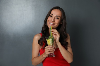 Young woman with refreshing drink on dark grey background