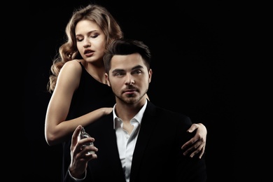 Passionate woman and handsome man using perfume on black background