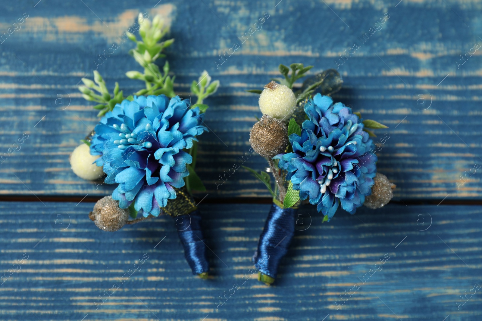 Photo of Stylish boutonnieres on blue wooden table, top view