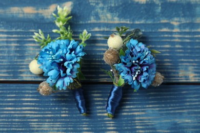 Stylish boutonnieres on blue wooden table, top view