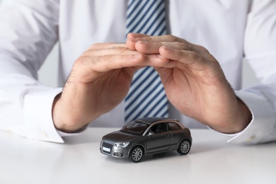 Photo of Male insurance agent covering toy car at table, closeup