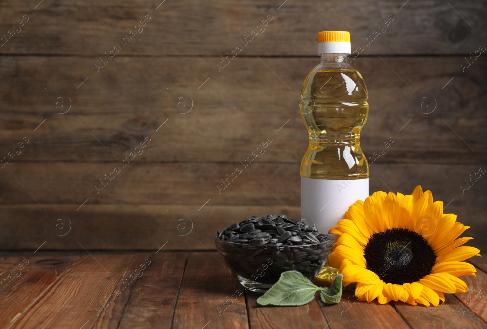 Photo of Sunflower cooking oil, seeds and yellow flower on wooden table, space for text