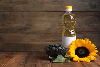 Sunflower cooking oil, seeds and yellow flower on wooden table, space for text