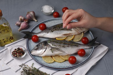 Woman salting raw dorado fish at grey table, closeup