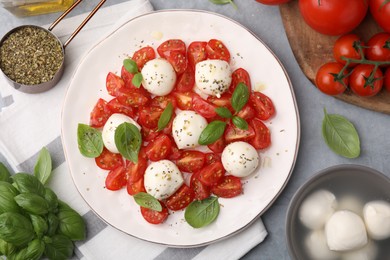 Photo of Tasty salad Caprese with tomatoes, mozzarella balls, basil and ingredients on grey background, flat lay