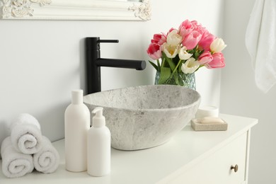 Vase with beautiful pink tulips and toiletries near sink in bathroom