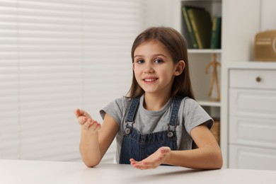 Cute little girl at white table indoors