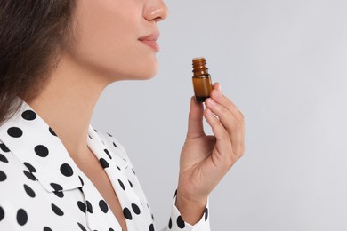 Photo of Woman with bottle of essential oil on light grey background, closeup