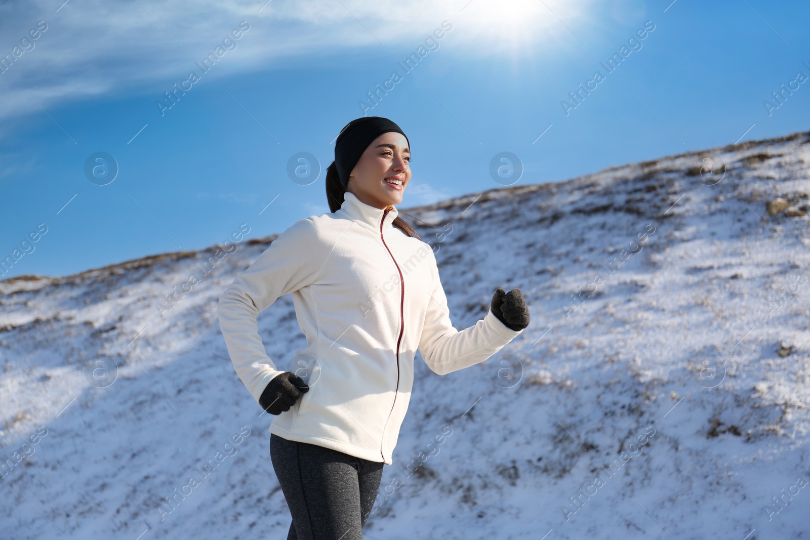 Photo of Happy woman running past snowy hill in winter. Outdoors sports exercises