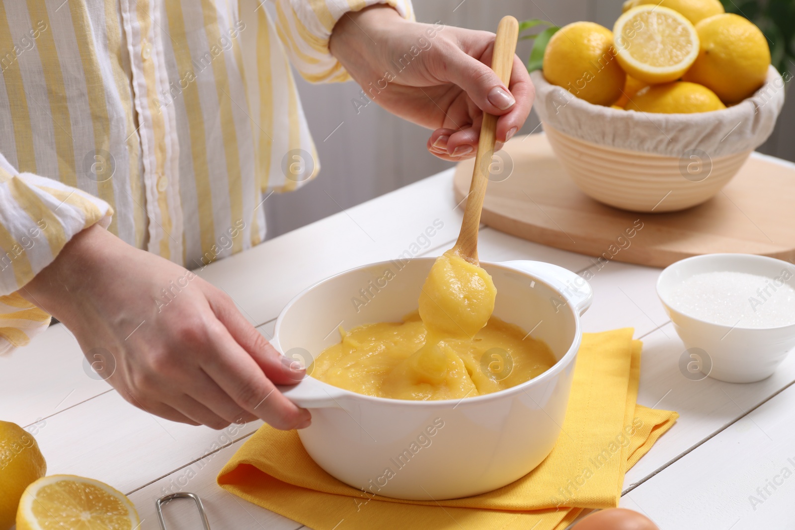 Photo of Woman cooking lemon curd at white wooden table, closeup