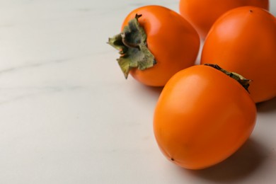 Photo of Delicious ripe persimmons on white marble table, space for text