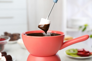 Dipping marshmallow into pot with chocolate fondue on table