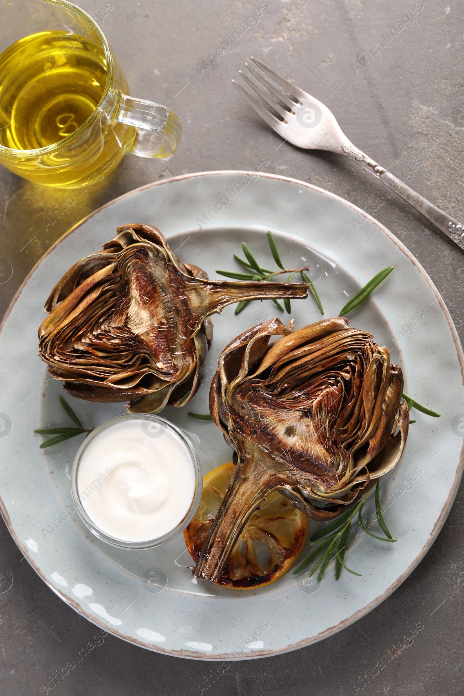 Photo of Plate with tasty grilled artichoke served on grey table, flat lay