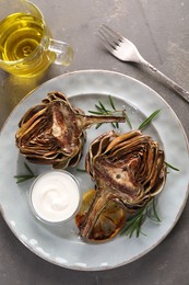 Photo of Plate with tasty grilled artichoke served on grey table, flat lay