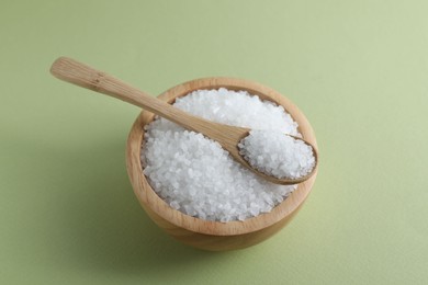 Photo of Organic white salt in bowl and spoon on olive background, above view