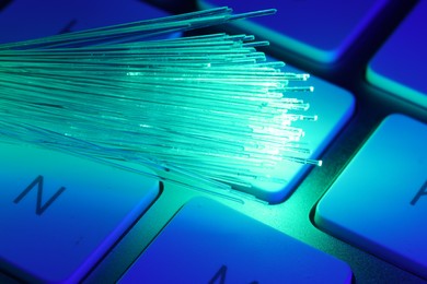 Photo of Optical fiber strands transmitting green light on computer keyboard, macro view