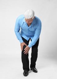 Full length portrait of senior man having knee problems on grey background