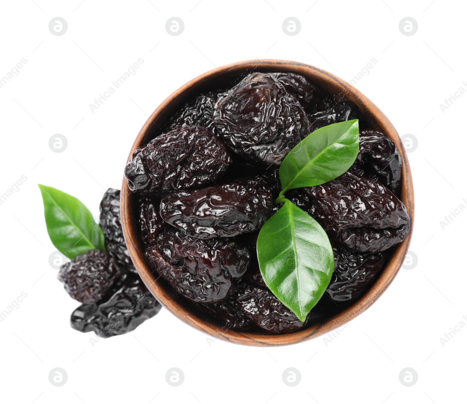 Photo of Bowl with sweet dried prunes and green leaves on white background, top view