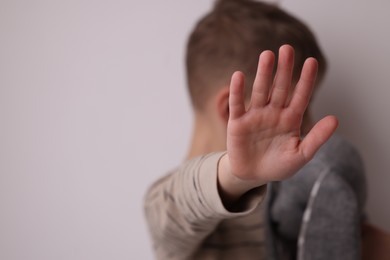 Photo of Child abuse. Boy doing stop gesture on light grey background, selective focus and space for text